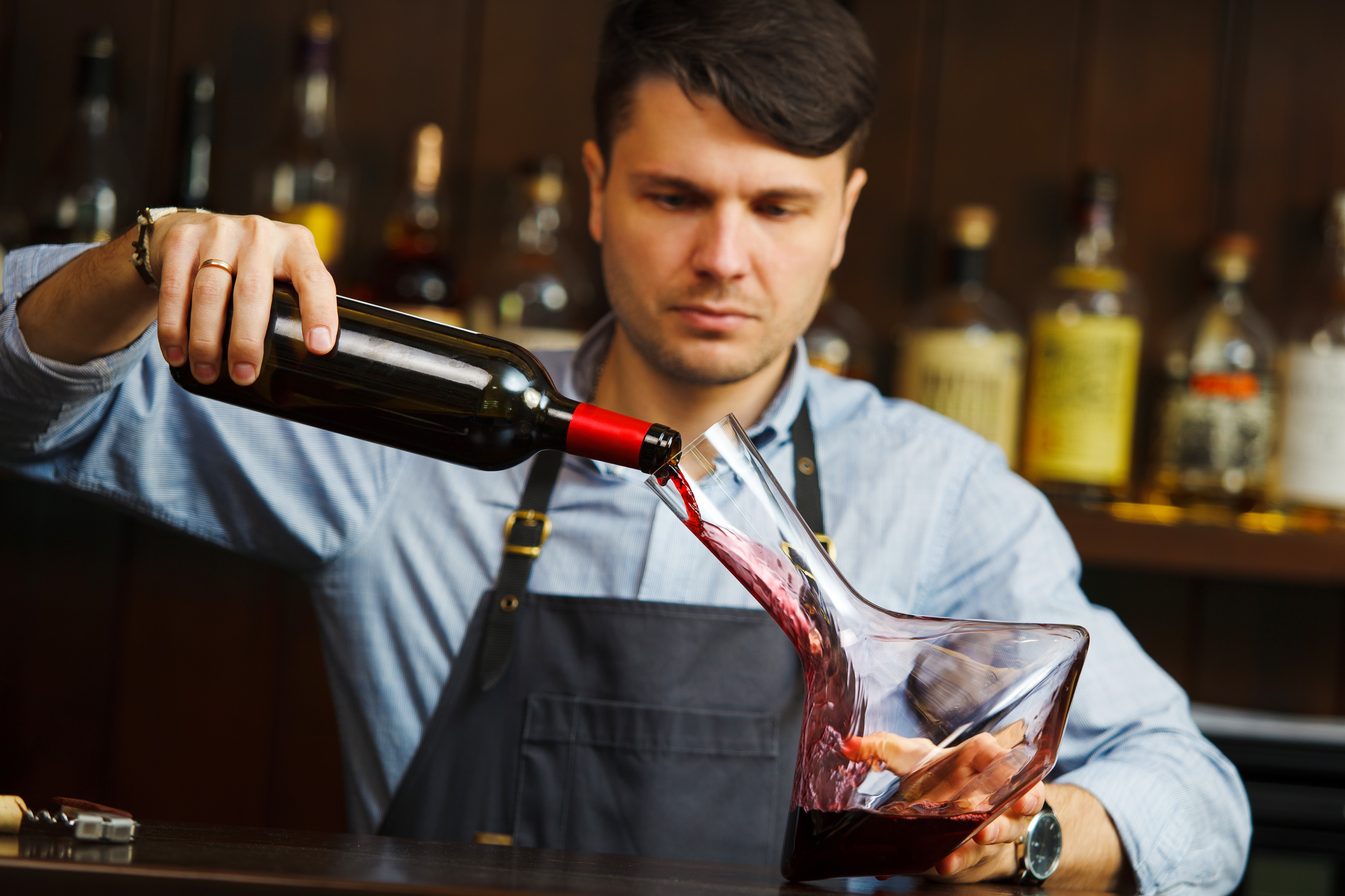 Männliche Servicekraft gießt Rotwein in einen Dekanter