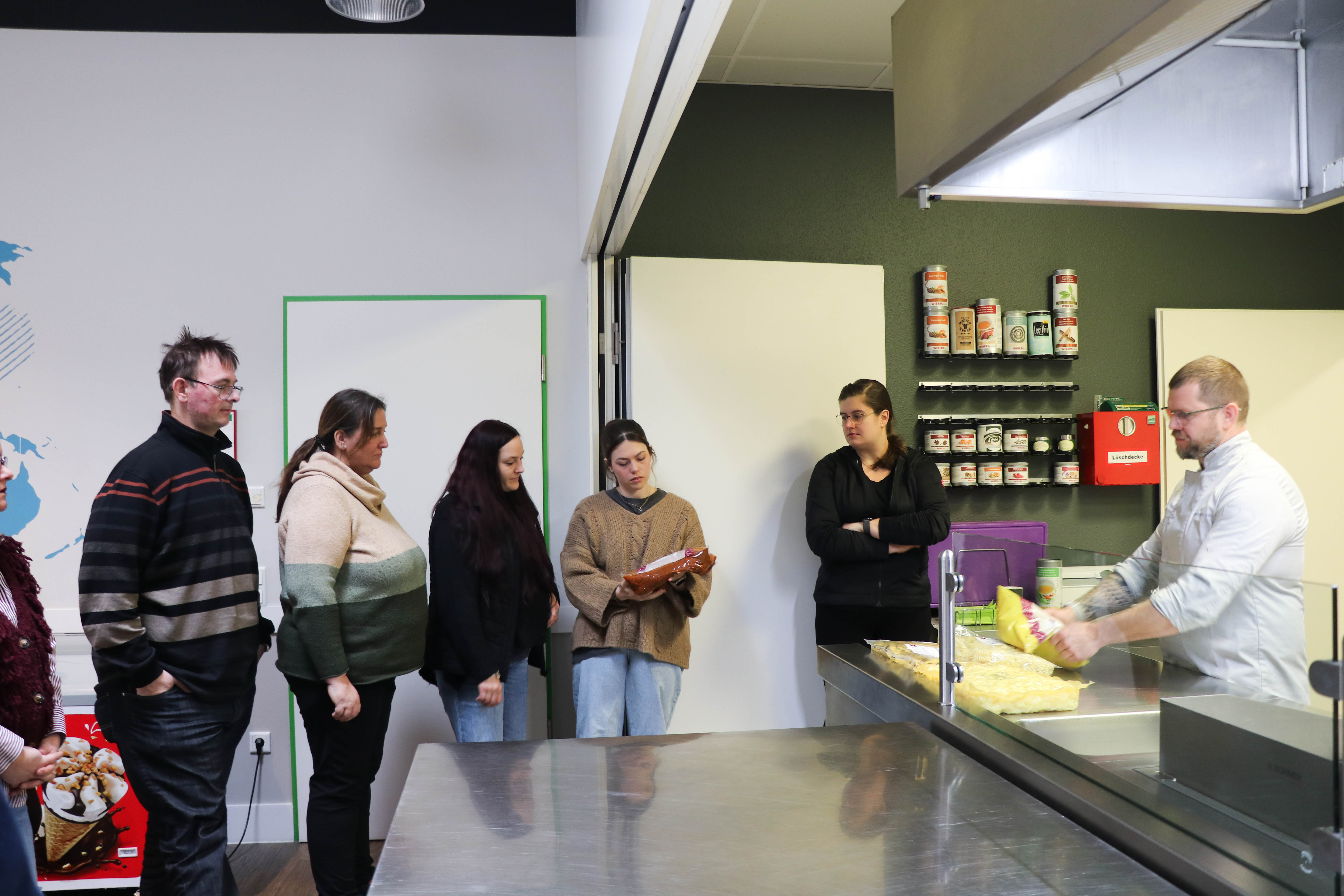 Eine Gruppe von Menschen sitzt an Tischen in einem Raum mit Projektorleinwand.