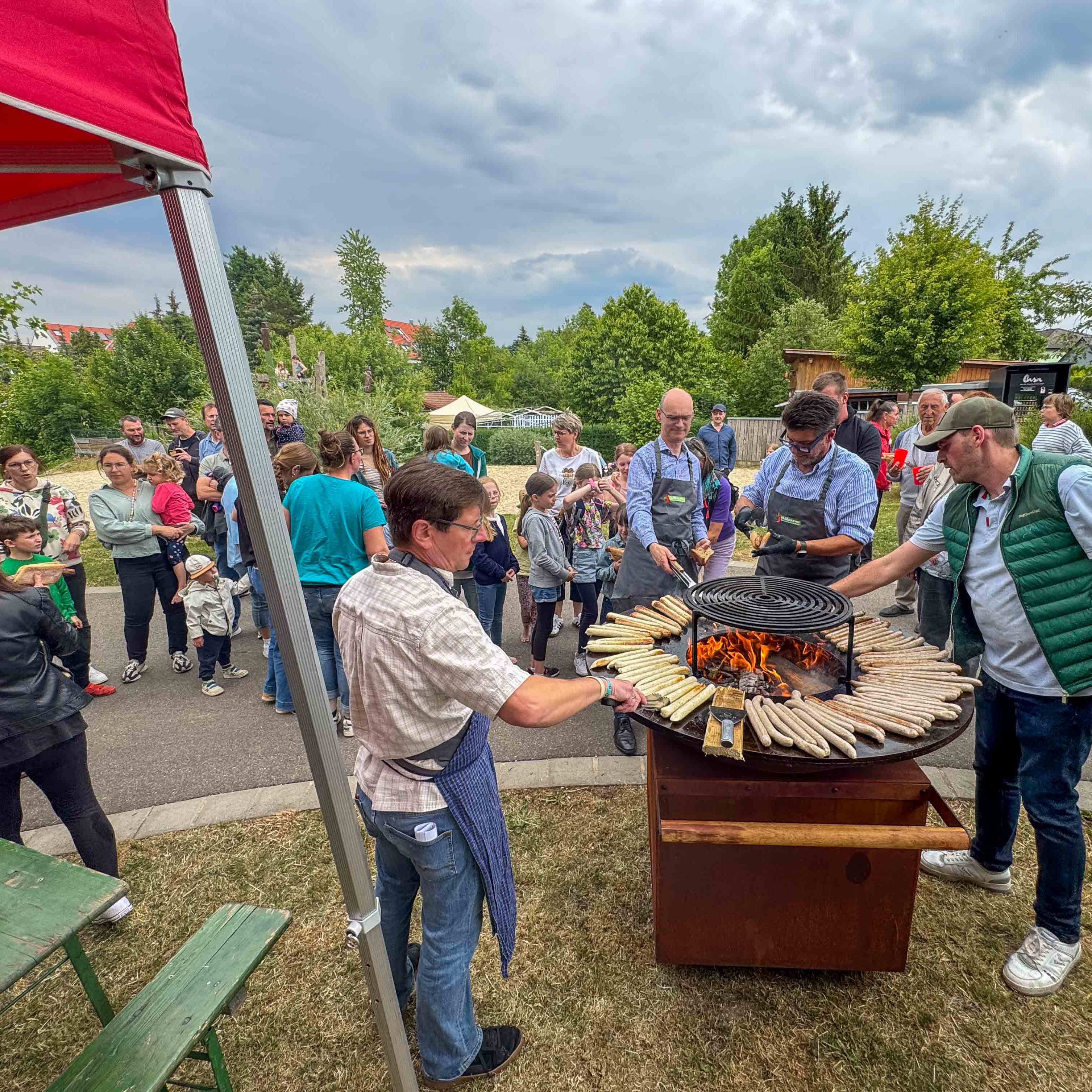 Eine Gruppe von Menschen steht um einen Grill im Freien. Eine Gruppe von Menschen steht um einen Grill im Freien.