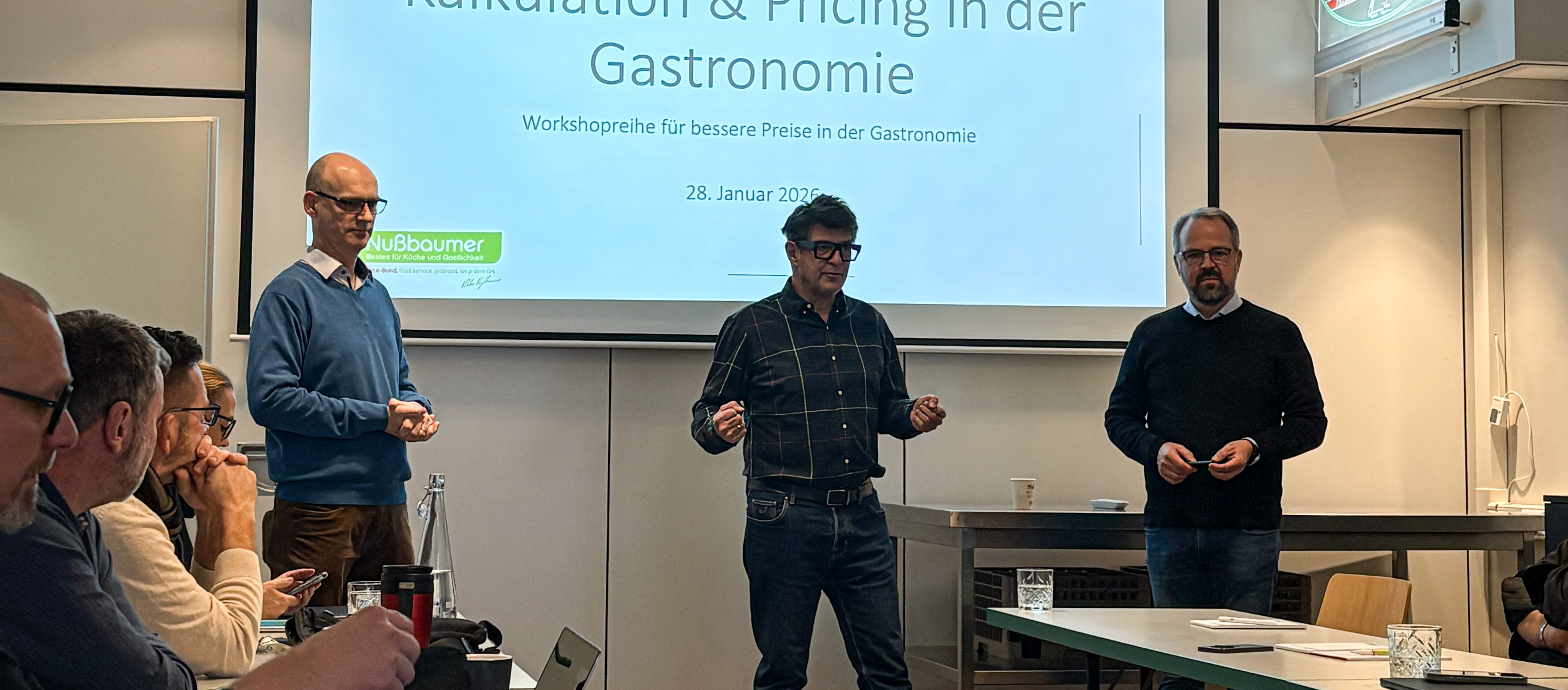 Eine Gruppe von Menschen in einem Raum mit Projektionsleinwand.