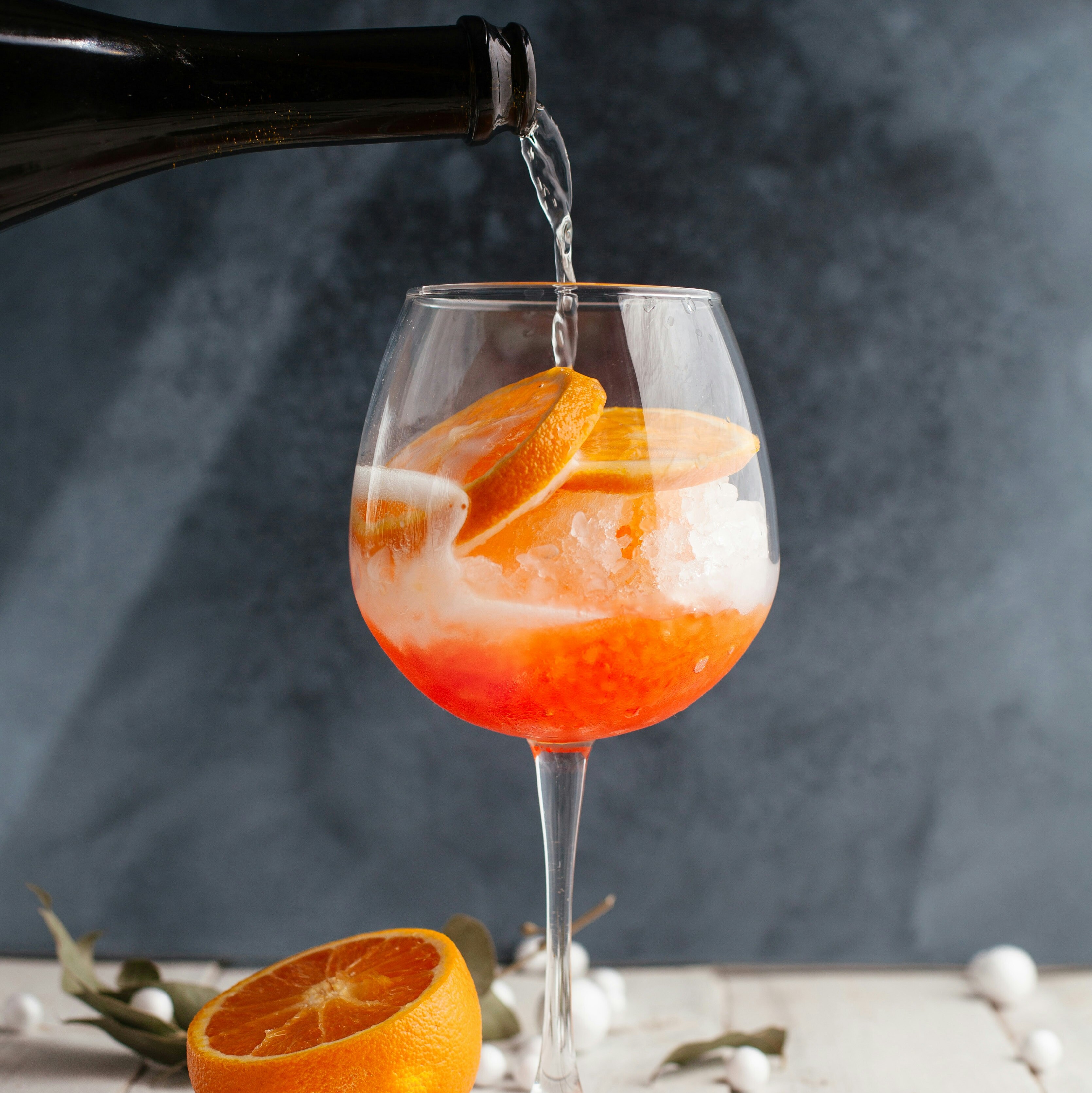Cocktailglas mit Aperol, eine Flasche schenkt Sekt ein