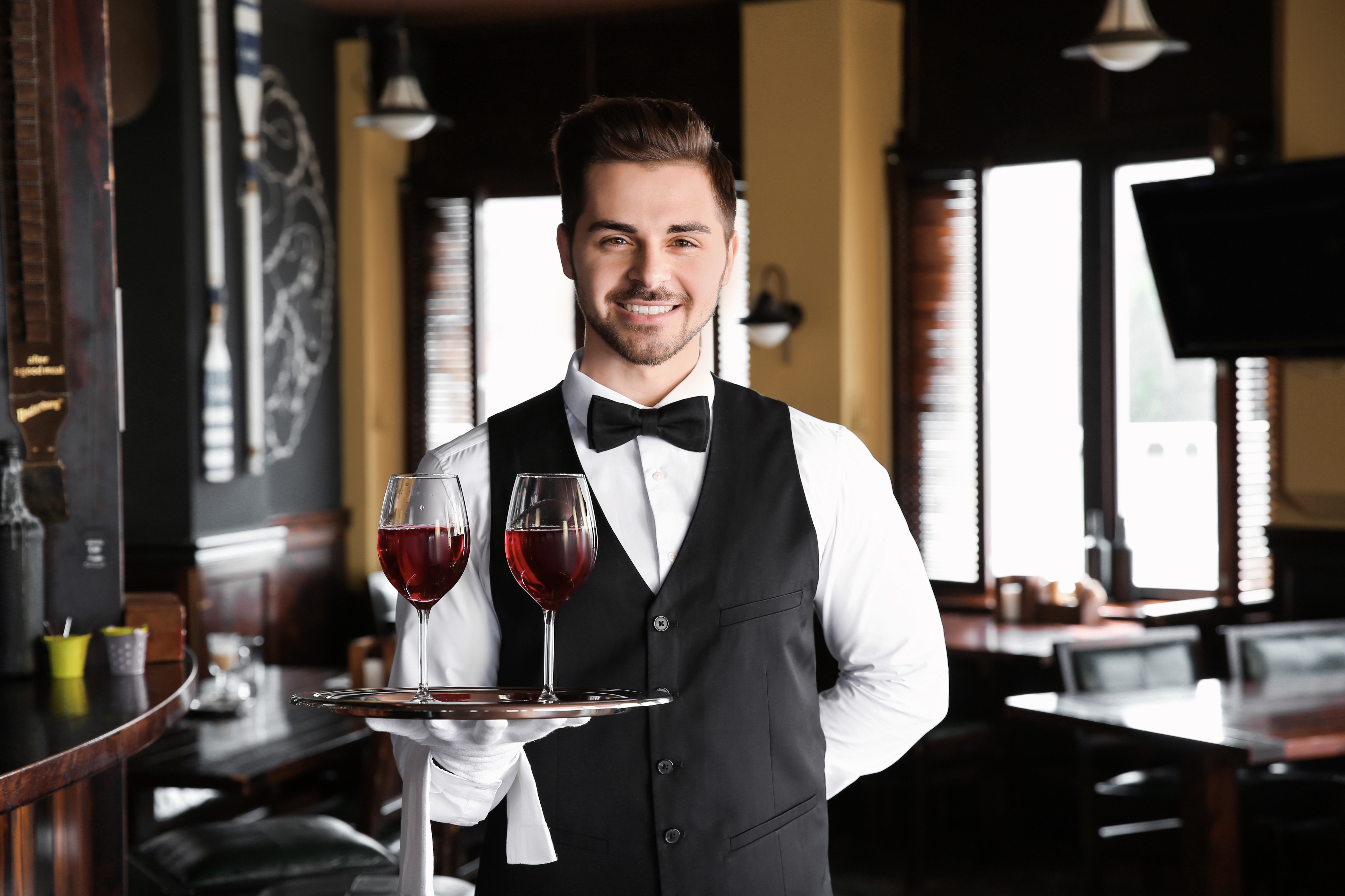 Junge, männliche Servicekraft mit Weingläsern im Restaurant