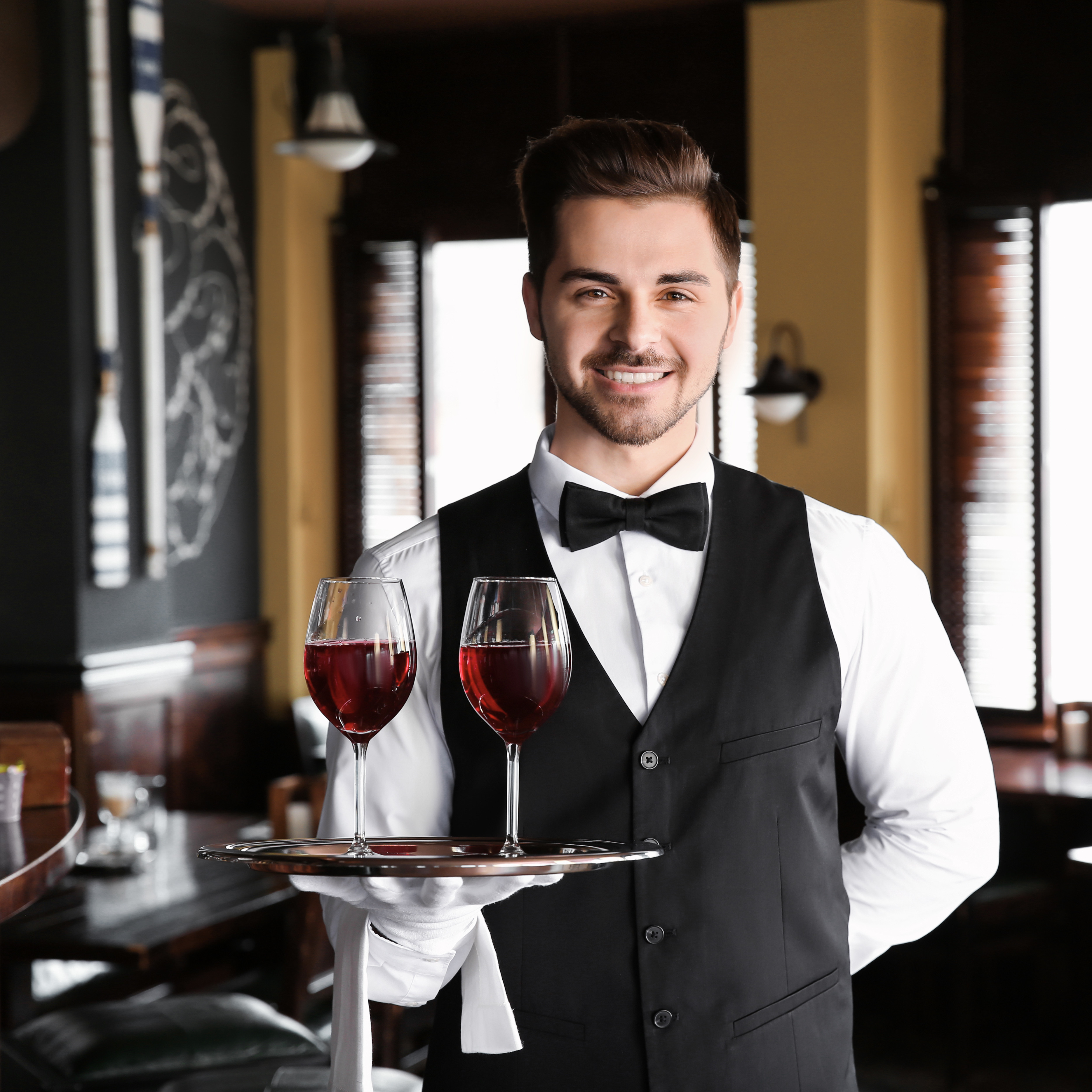 Junger männlicher Servicemitarbeiter mit Weingläsern im Restaurant