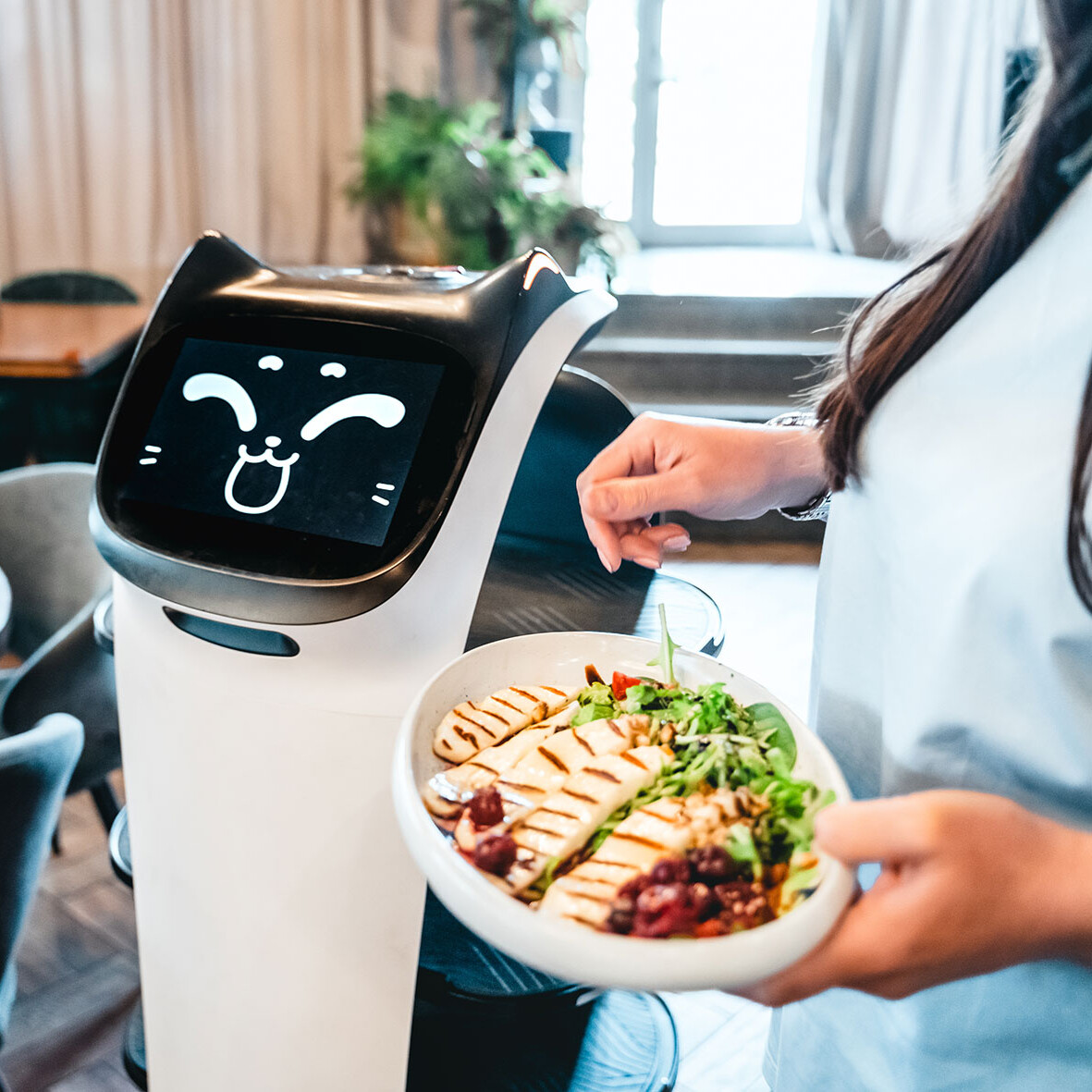 Pflegerin mit Serviceroboter Eine Person hält eine Schüssel mit Essen. Daneben steht ein Serviceroboter.