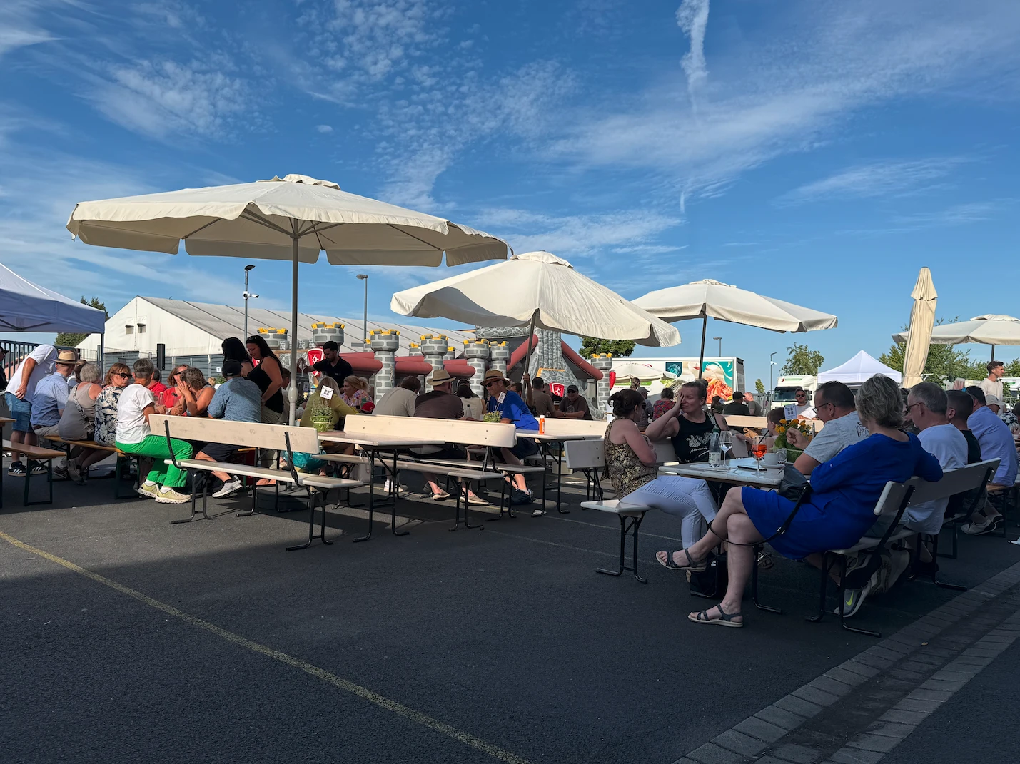 Nußbaumer Sommerfest Eine Gruppe von Menschen sitzt an Tischen unter Sonnenschirmen.