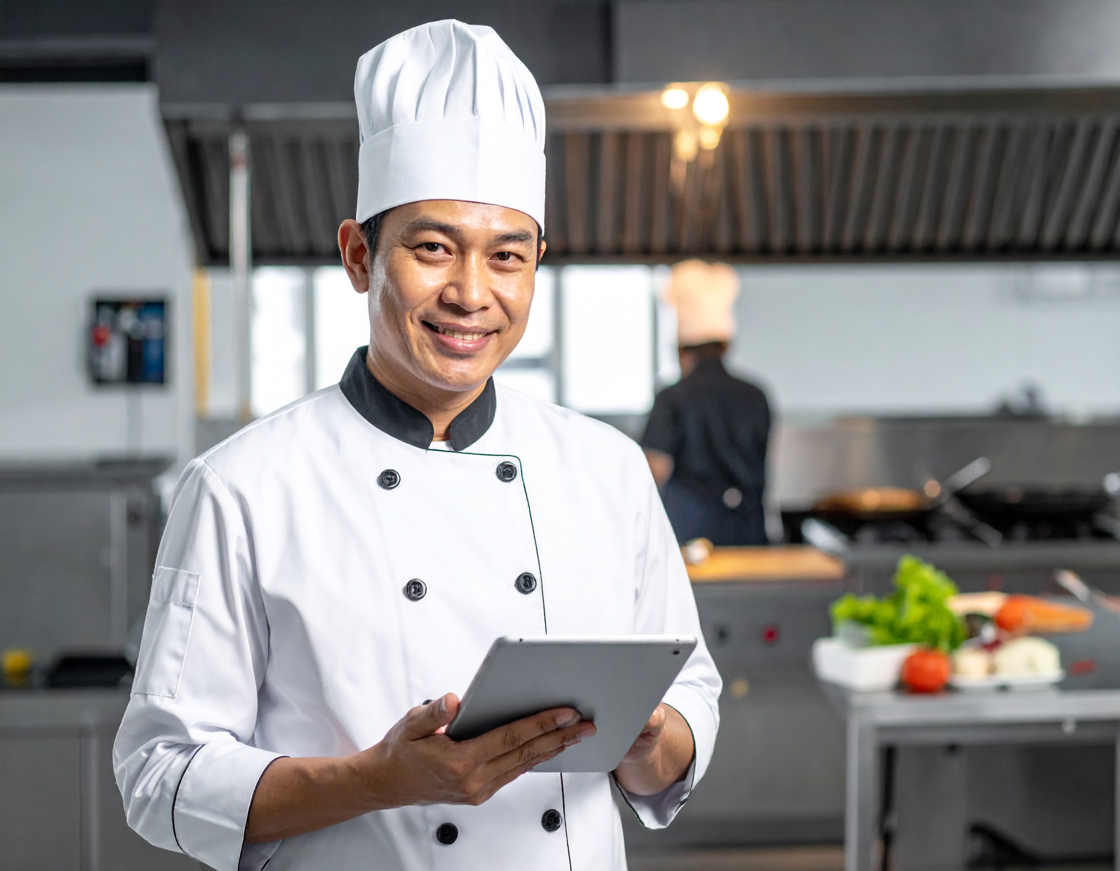Ein Mann in Kochuniform hält ein Tablet. Ein Mann in Kochuniform hält ein Tablet.