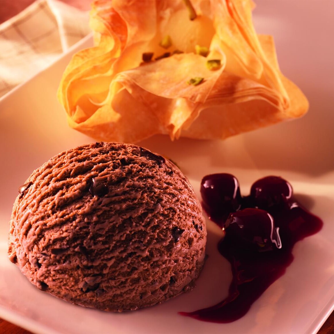 Birne im Filonest mit Schokoladeneis und Dessertkirschen auf einem Teller angerichtet