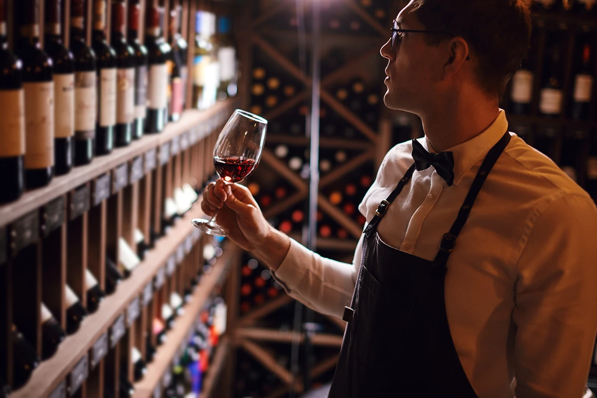 Sommelier steht im Weinkeller und hält ein Glas Wein in der Hand Sommelier steht im Weinkeller und hält ein Glas Wein in der Hand