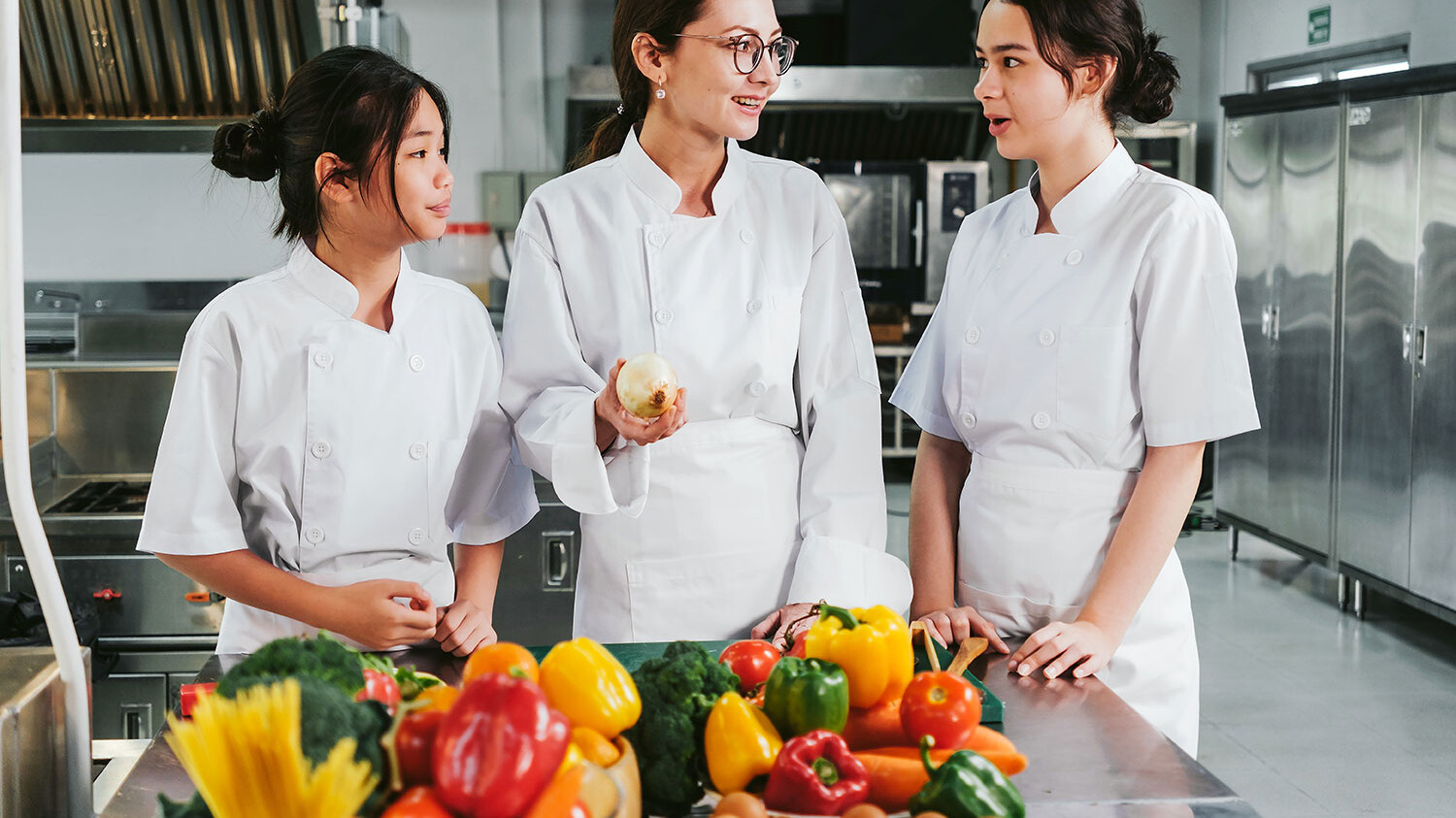 Eine Gruppe von Frauen in weißen Kochjacken steht in einer Küche.