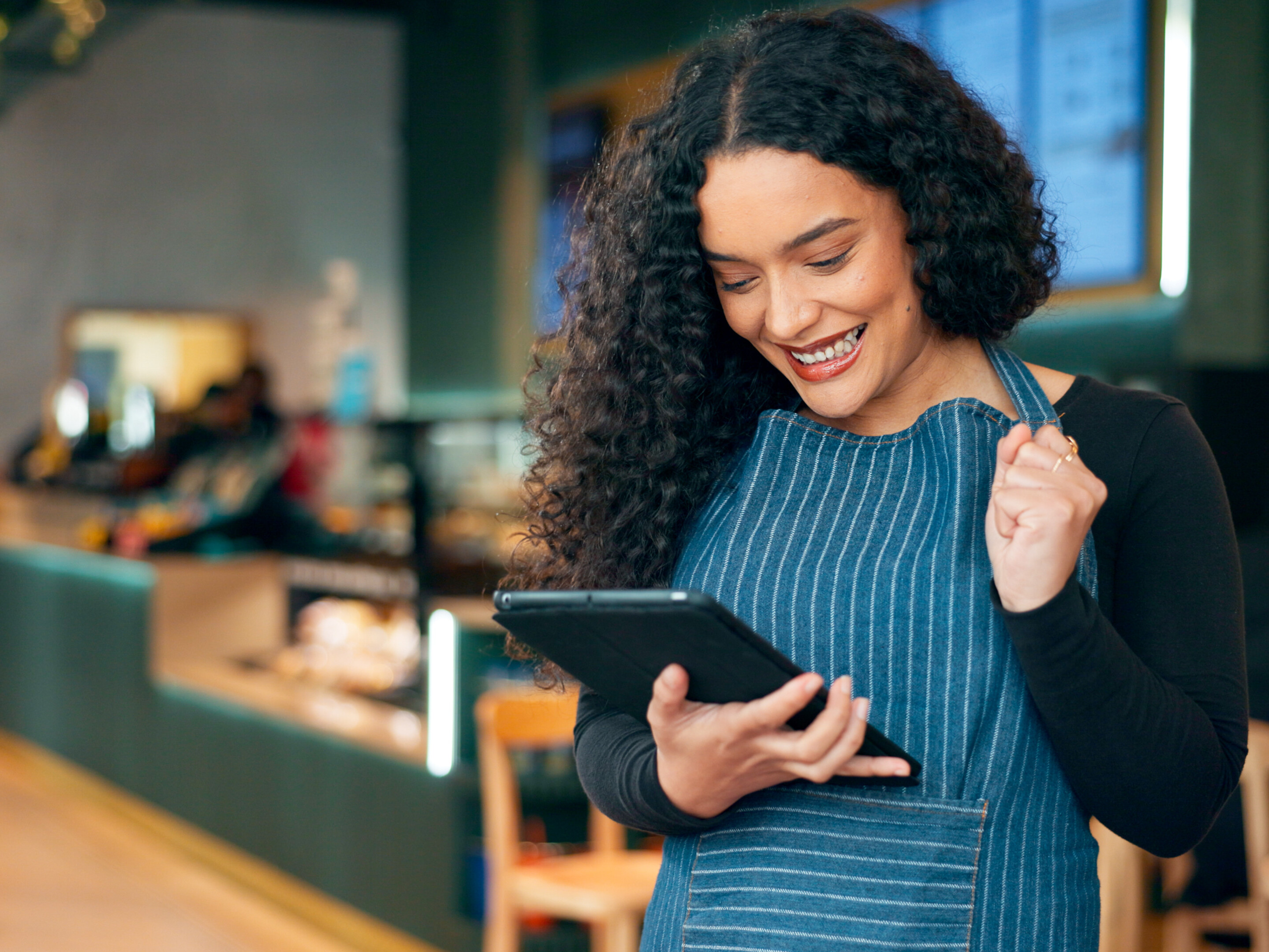 Eine Frau trägt eine Schürze und hält ein Tablet auf dem sie eine Kundenbewertung liest.