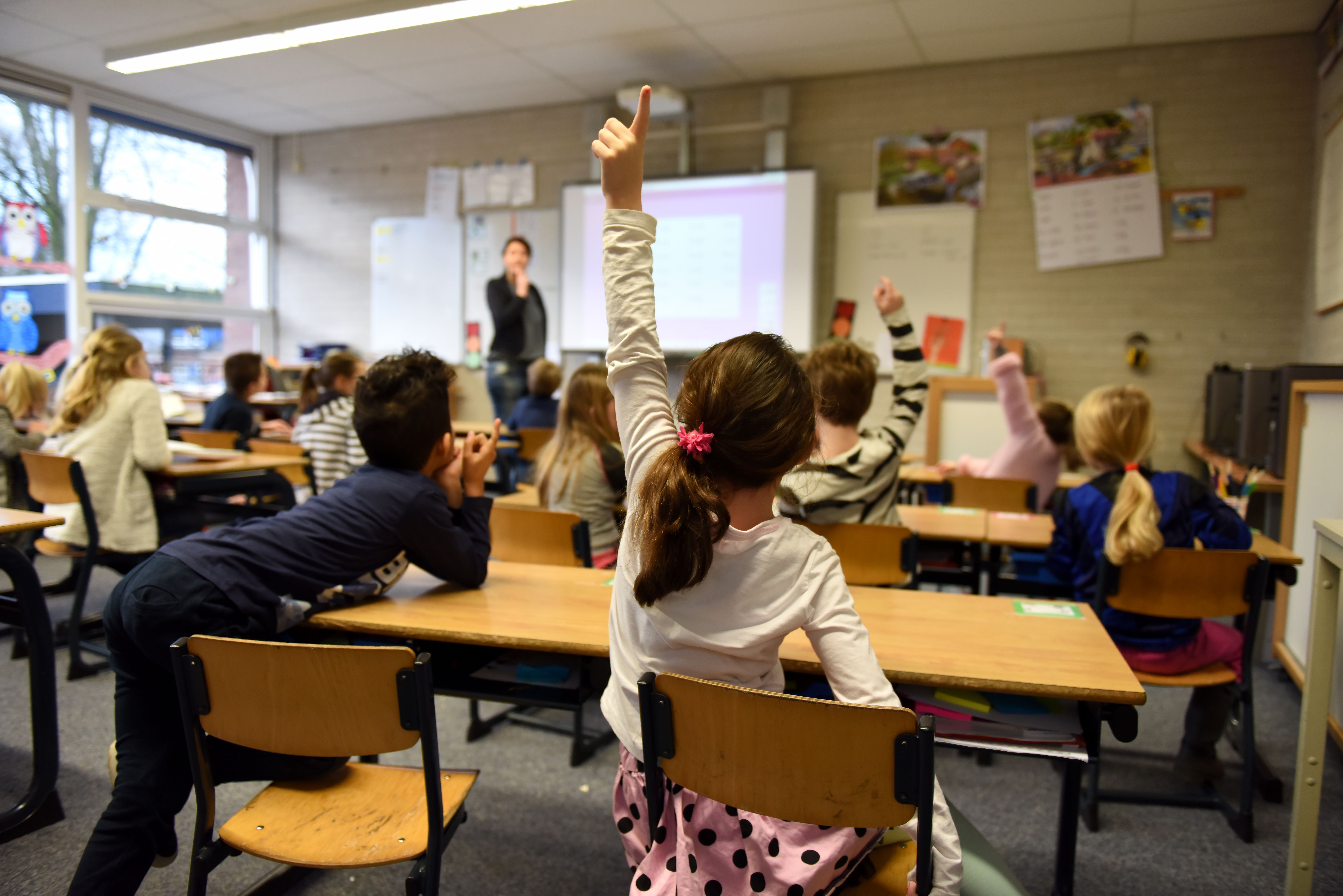 Eine Gruppe von Kindern im Klassenzimmer hebt die Hände.