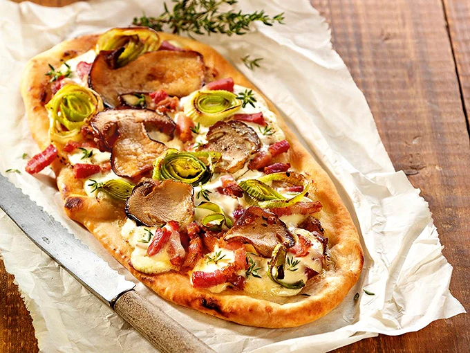 Flammkuchen mit Speck und Gemüse auf einem Papiertuch